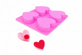 Pink silicone heart mold with four heart-shaped red candies on a white background
